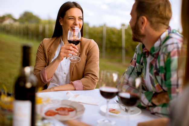 Grupo de jóvenes sentados a la mesa y bebiendo vino tinto en el viñedo