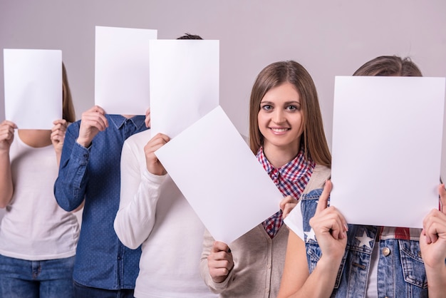 Foto grupo de jóvenes sosteniendo una pizarra y cubrir sus rostros.