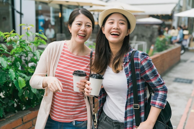Un grupo de jóvenes turistas pasean por las calles del casco antiguo. amigas viajeras sosteniendo vasos de papel con café en las manos en un cálido día de verano. Buen humor dos damas riéndose mirando a un lado.