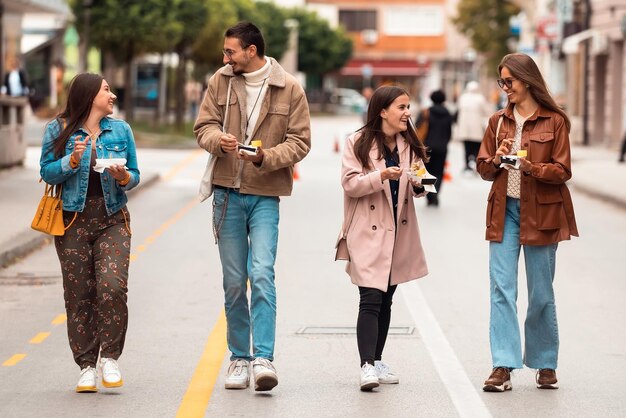 Un grupo de jóvenes vestidos con ropa moderna hablan mientras caminan por la ciudad y comen dulces Enfoque selectivo