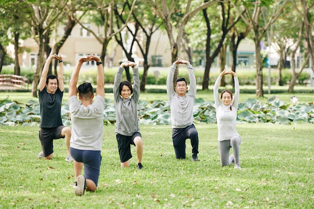 Grupo de jóvenes vietnamitas en forma siguiendo al entrenador al hacer ejercicio en el parque de la ciudad