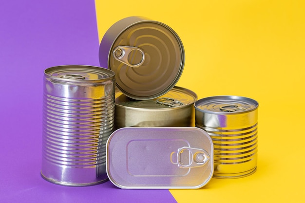 Un grupo de latas de hojalata apiladas con bordes en blanco en un fondo amarillo y violeta dividido