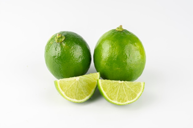 Grupo de limones verdes con limón en rodajas sobre fondo blanco.