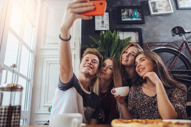 Grupo de lindos adolescentes tomando selfie con celular mientras se sientan en un restaurante con interior en estilo retro