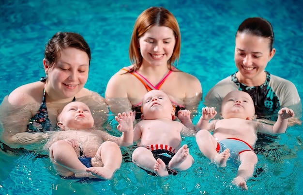 Foto un grupo de madres con sus hijos pequeños en una clase de natación infantil con un entrenador.