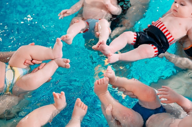 Un grupo de madres con sus hijos pequeños en una clase de natación para niños con un entrenador.