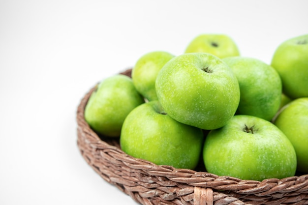 Grupo de manzanas verdes maduras en una canasta sobre superficie blanca