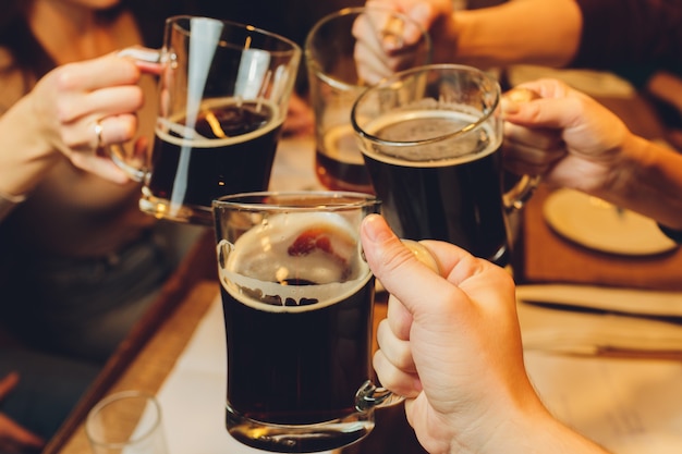 Grupo masculino tilintar de copos de cerveja escura e clara à mesa.