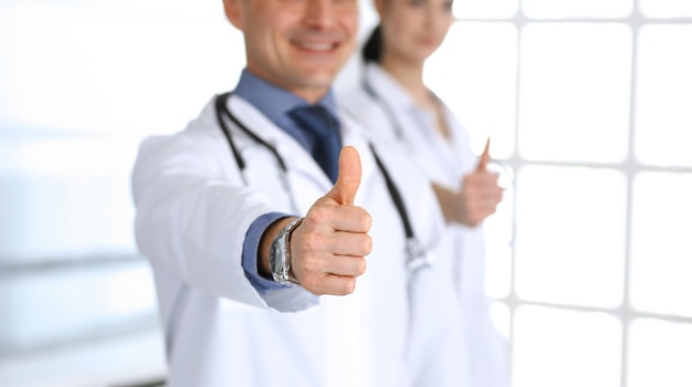 Grupo de médicos alegres sonriendo a la cámara, pulgares arriba. Perfecto servicio médico en clínica. Futuro feliz en medicina y salud.