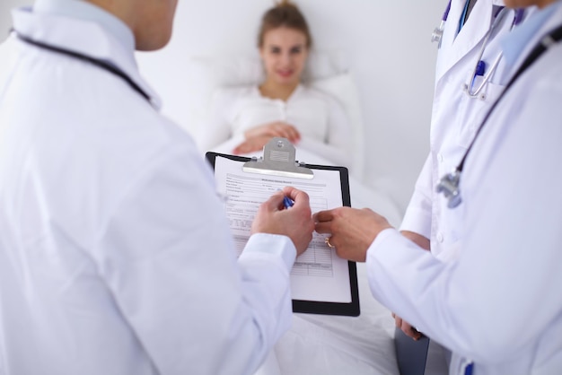 Un grupo de médicos discutiendo el historial médico de cerca, un paciente sonriente feliz en el fondo.