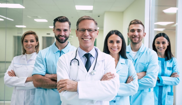 Grupo de médicos modernos exitosos y seguros están posando y mirando a la cámara en el pasillo del hospital