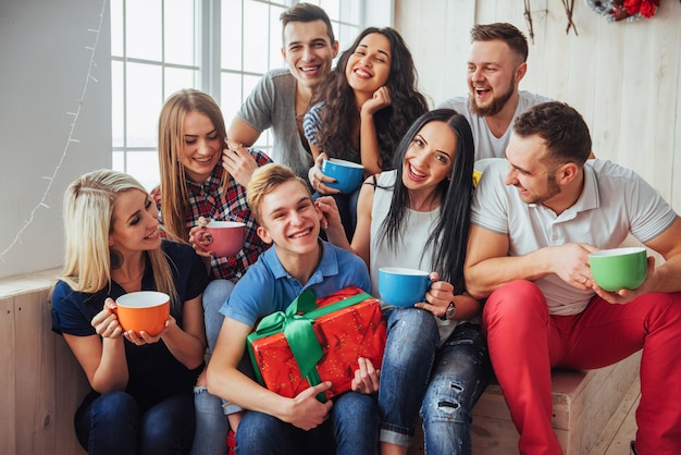 Grupo de mejores amigos en la fiesta. gente sonriente y alegre sentada en las escaleras una taza de café saluda el cumpleaños, gran regalo