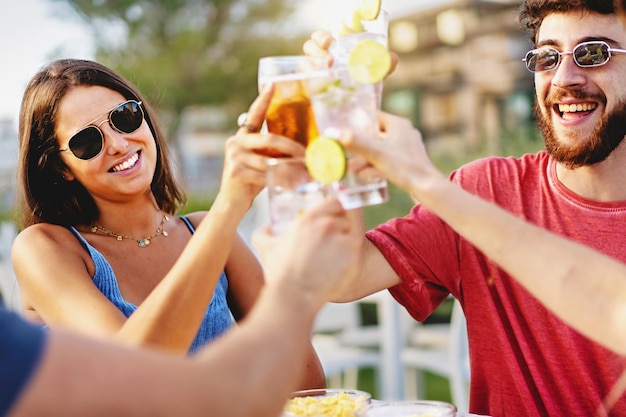 Grupo de millenials brindando al aire libre sentados en la terraza de un bar quiosco de verano