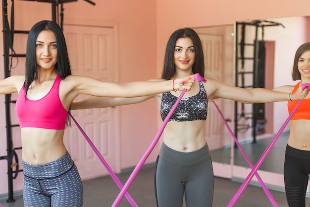 Grupo de mujeres alegres jóvenes haciendo ejercicios con cinta de goma fitness