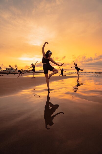 Un grupo de mujeres asiáticas está de pie en la playa vestida de negro y haciendo movimientos de ballet al unísono