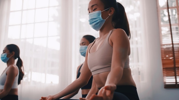 Un grupo de mujeres asiáticas con máscaras médicas mientras hacen ejercicio de yoga en el gimnasio.