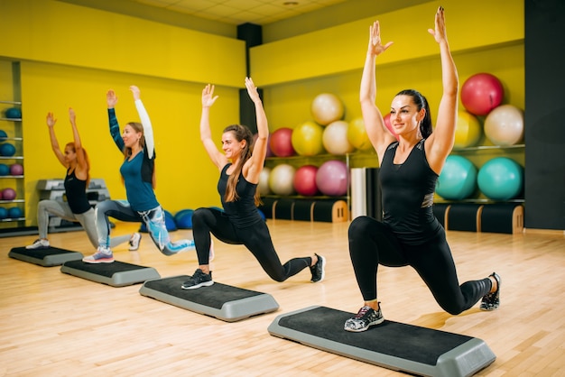 Grupo de mujeres en entrenamiento aeróbico escalonado. Trabajo en equipo de deporte femenino en el gimnasio. Fit class, ejercicio físico en movimiento