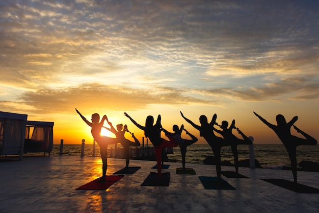 El grupo de mujeres haciendo yoga al amanecer cerca del mar.