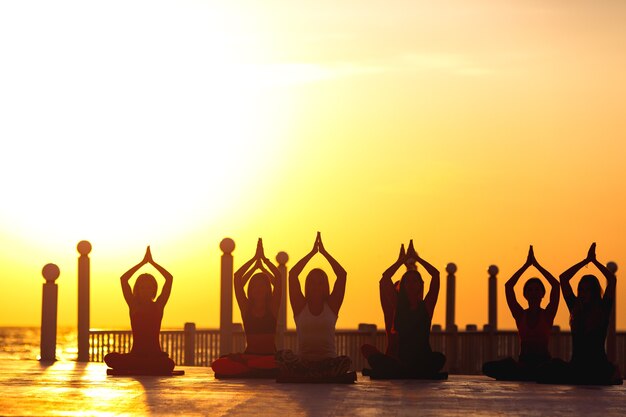 El grupo de mujeres haciendo yoga al amanecer cerca del mar.