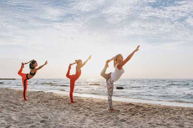 El grupo de mujeres haciendo yoga al amanecer cerca del mar.