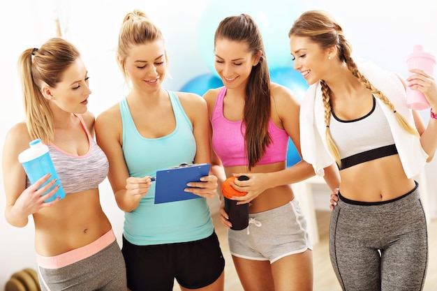 Grupo de mujeres jóvenes discutiendo el plan de entrenamiento en el gimnasio.