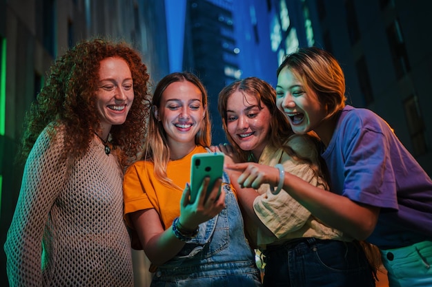 Grupo de mujeres jóvenes divirtiéndose compartiendo medios en las redes sociales con un teléfono móvil en la noche tres