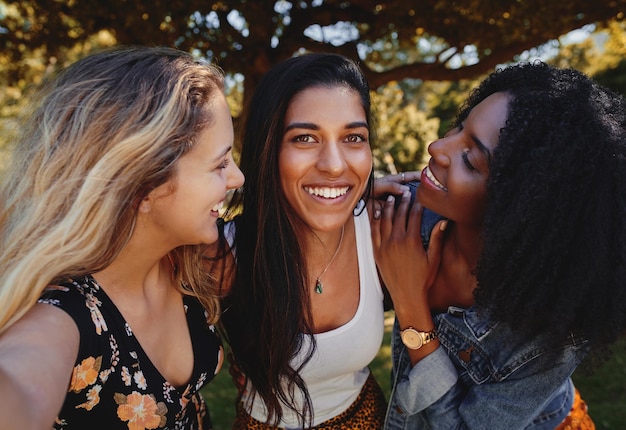 Un grupo de mujeres jóvenes emocionadas posando entre amigas encantadoras con ropa de moda tomando selfies. Niñas jóvenes tomando selfies en un parque en un día soleado.