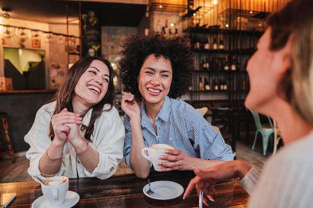 Un grupo de mujeres jóvenes hablando y riendo sentadas en una cafetería o restaurante dos damas