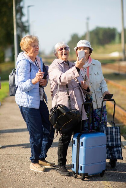 Un grupo de mujeres mayores sonrientes se toman un autorretrato en una plataforma esperando un tren para viajar durante una pandemia de COVID-19