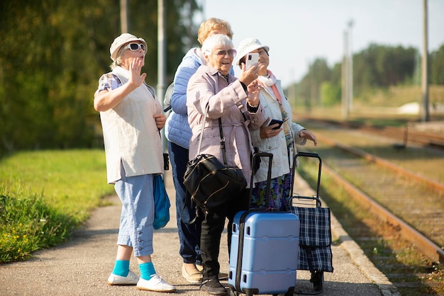Un grupo de mujeres mayores sonrientes se toman un autorretrato en una plataforma esperando un tren para viajar durante una pandemia de COVID-19