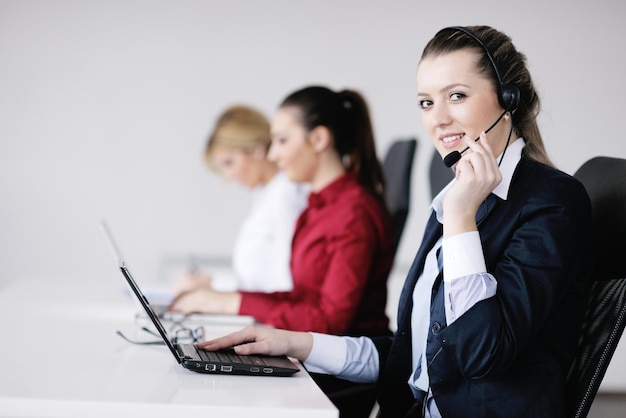 Un grupo de mujeres de negocios bastante jóvenes con auriculares sonriéndote contra el fondo blanco