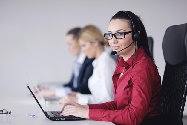 Un grupo de mujeres de negocios bastante jóvenes con auriculares sonriéndote contra el fondo blanco