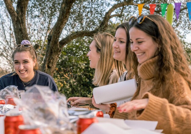 Grupo de mujeres riendo mientras cuentan anécdotas en la mesa durante una fiesta al aire libre