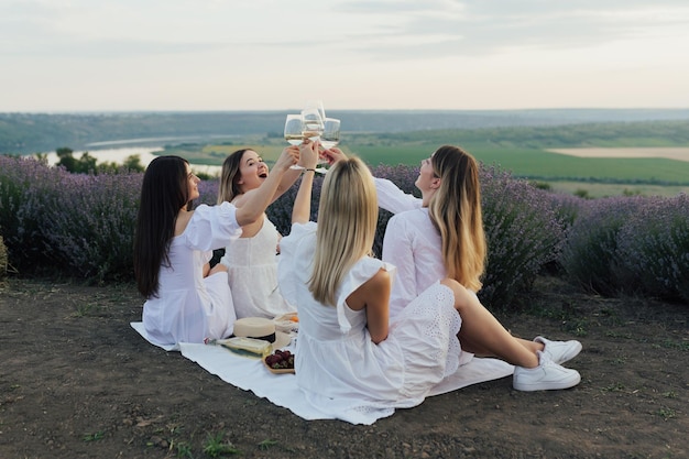 Un grupo de mujeres vestidas de blanco están sentadas sobre una manta con un campo de lavanda al fondo.