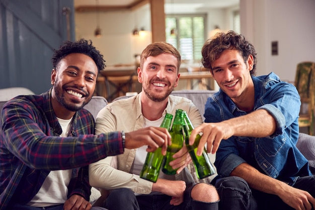 Grupo multicultural de amigos do sexo masculino no sofá em casa bebendo cerveja e fazendo brindes com garrafas