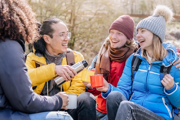 Grupo multicultural de caminhantes sentados no topo da montanha bebendo café com mochilas Amigos hipster felizes tendo um dia de trekking juntos Conceito de viagem e acampamento