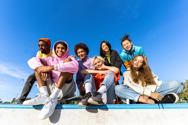 Grupo multicultural de jovens amigos se divertindo ao ar livre e se divertindo - adolescentes elegantes e descolados se reunindo no parque urbano de skate