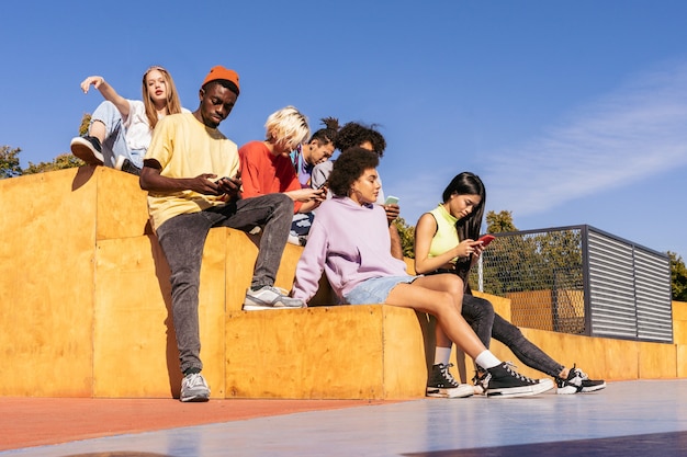 Grupo multicultural de jóvenes amigos que se unen al aire libre y se divierten - Adolescentes elegantes y geniales reunidos en un parque de patinaje urbano