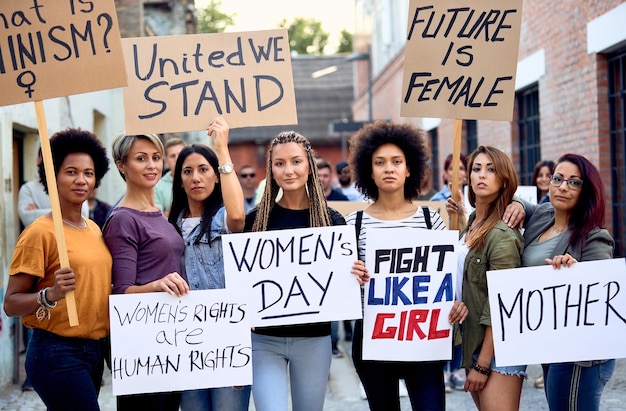 Grupo multiétnico de activistas que protestan por los derechos de las mujeres en las calles de la ciudad mientras los hombres están parados en el fondo