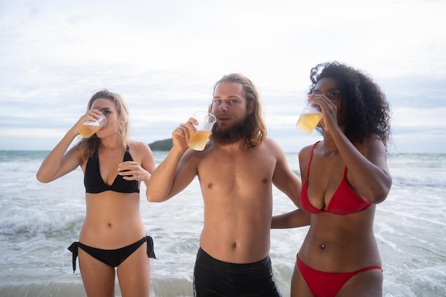 Grupo multiétnico de amigos divirtiéndose en la playa bebiendo cerveza y divirtiéndose