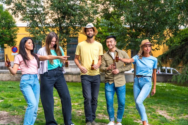 Grupo multiétnico de amigos de fiesta en un parque de la ciudad con botellas de cervezas