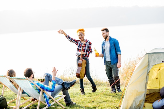 Grupo multiétnico de amigos vestidos casualmente divirtiéndose durante la recreación al aire libre en el campamento cerca del lago