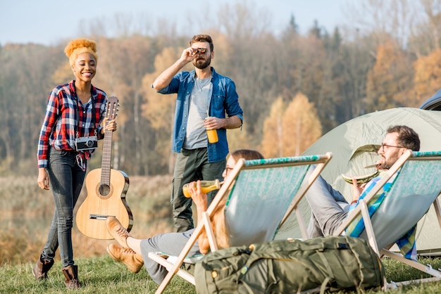 Grupo multiétnico de amigos vestidos casualmente divirtiéndose durante la recreación al aire libre en el campamento cerca del lago