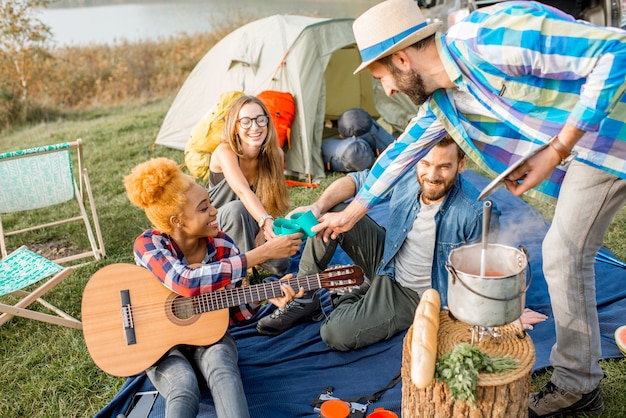 Grupo multiétnico de amigos vestidos casualmente tintineo de vasos durante la cena al aire libre en el camping