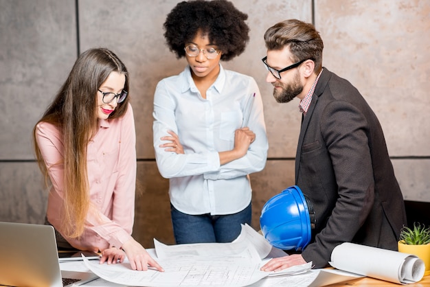 Grupo multiétnico de arquitectos o diseñadores que trabajan juntos en los planos arquitectónicos de la oficina.