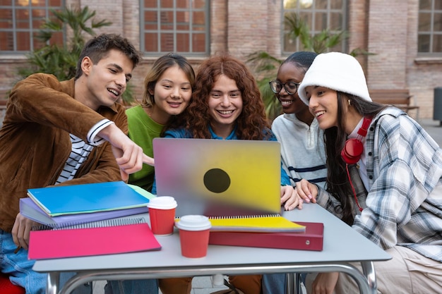 Un grupo multiétnico de cinco estudiantes con una computadora y notas se sientan cerca del campus para revisar el examen