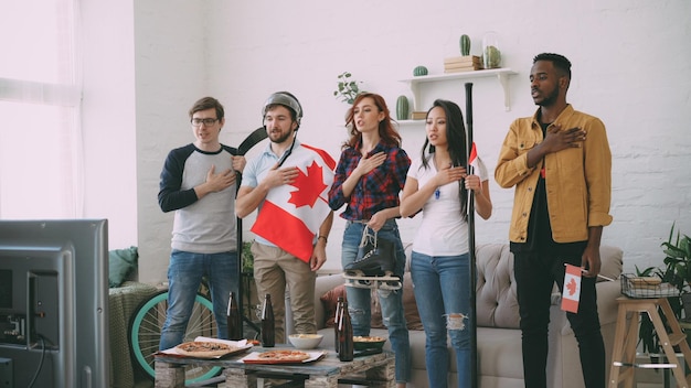 Grupo multiétnico de amigos ouvindo e cantando hino nacional canadense antes de assistir esportes