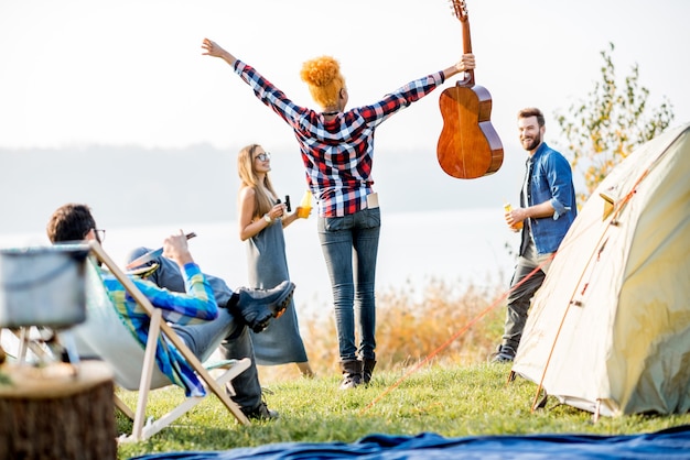 Grupo multiétnico de amigos vestidos casualmente se divertindo durante a recreação ao ar livre no acampamento perto do lago