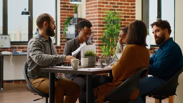 Grupo multiétnico de colegas reunidos no escritório da diretoria para fazer trabalho em equipe na apresentação do relatório de negócios. analisando informações de pesquisa de dados e gráficos com papéis, colaboração de inicialização.