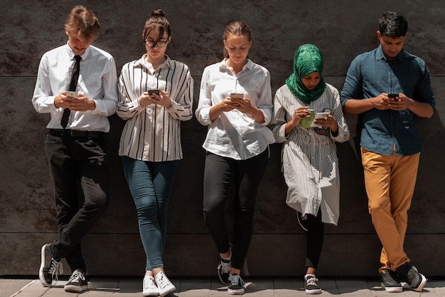 Grupo multiétnico de empresários casuais usando um smartphone durante uma pausa para o café do trabalho em frente à parede preta do lado de fora. Foto de alta qualidade
